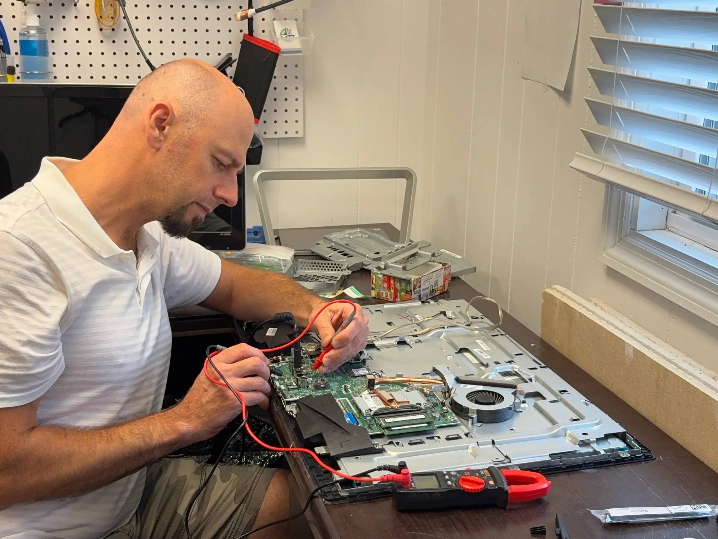 Yuriy probing a laptop board with a multimeter at the JY Computer Services repair bench