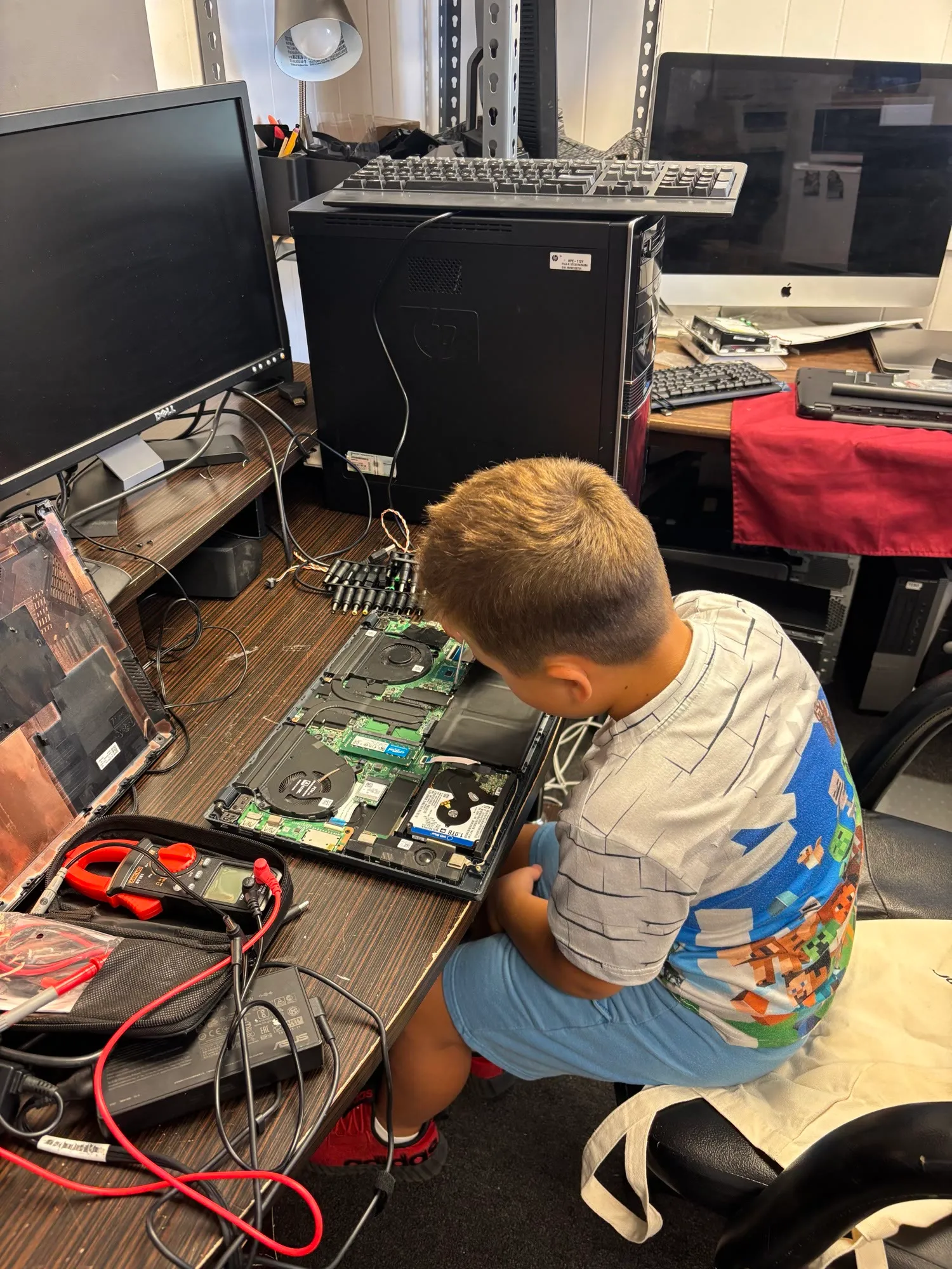 A young family member learning to work on a test laptop at the shop bench